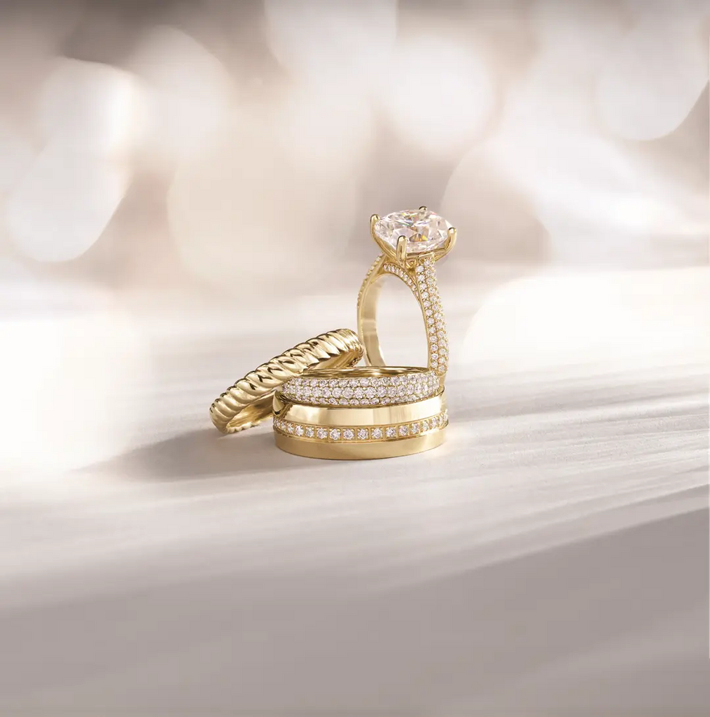 Stack of gold and diamond wedding bands with diamond engagement ring standing up next to it.