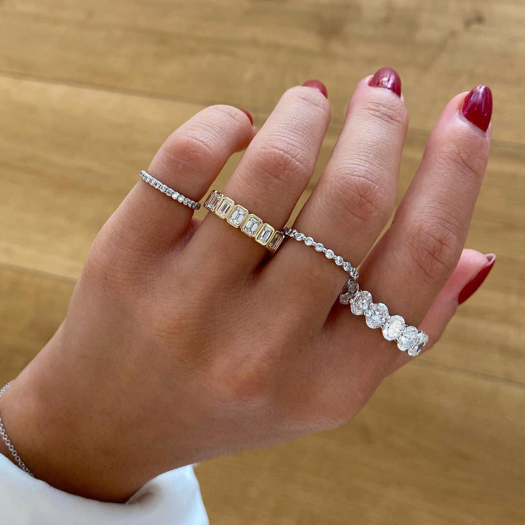 Hand wearing multiple diamond rings on a wooden surface