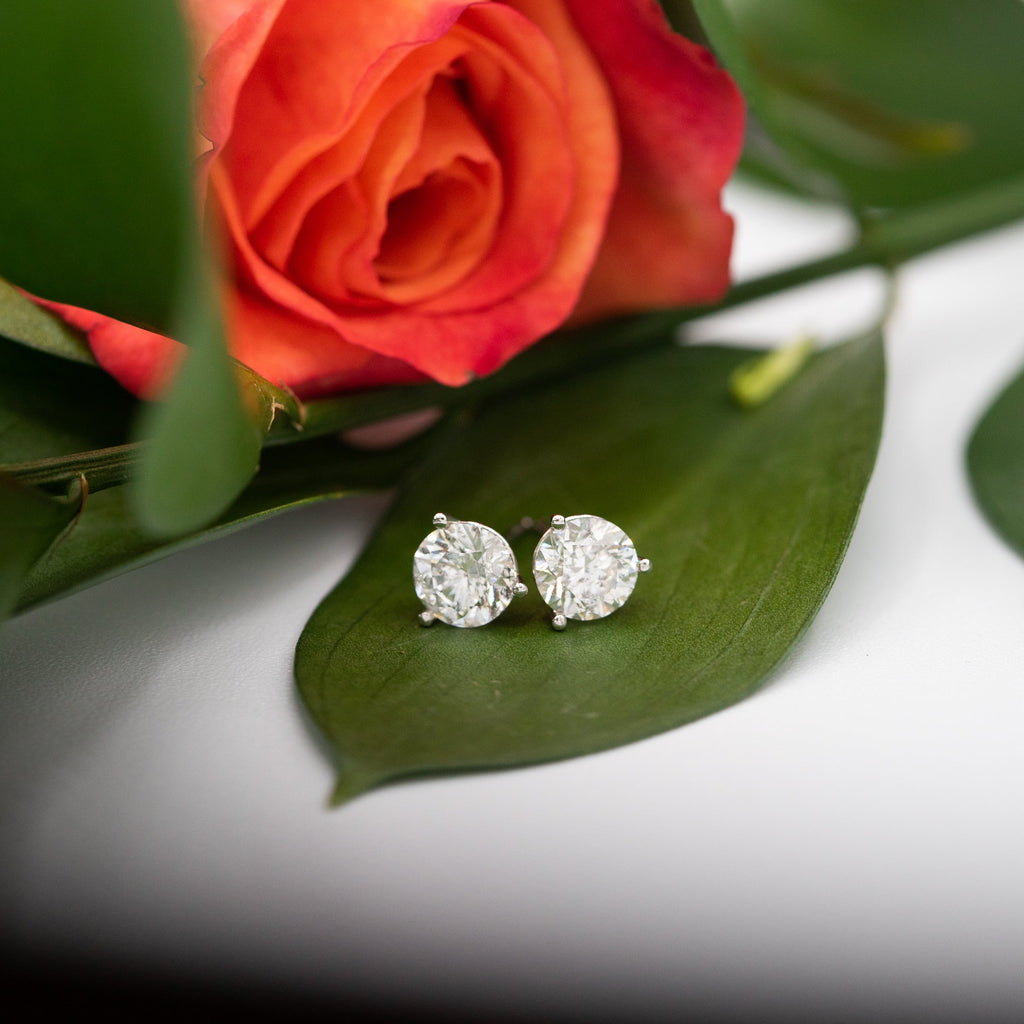 Diamond earrings on a green leaf with a blurred red rose in the background