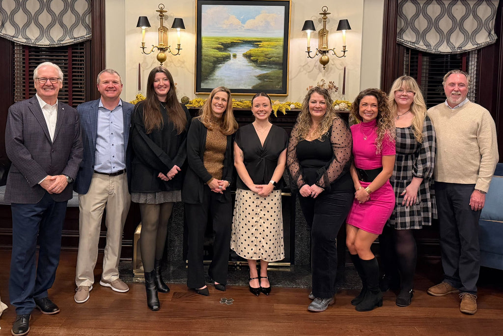 Group of people posing for a photo in a formal setting with a painting on the wall.