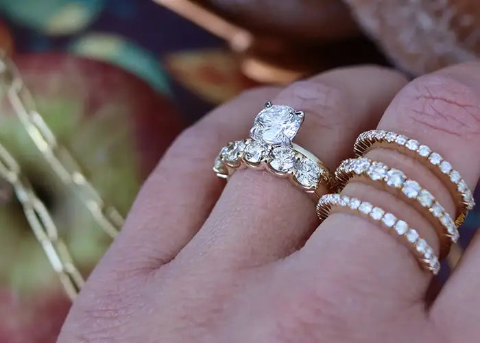 Engagement ring and wedding bands on woman's fingers. Apple and necklace in background.