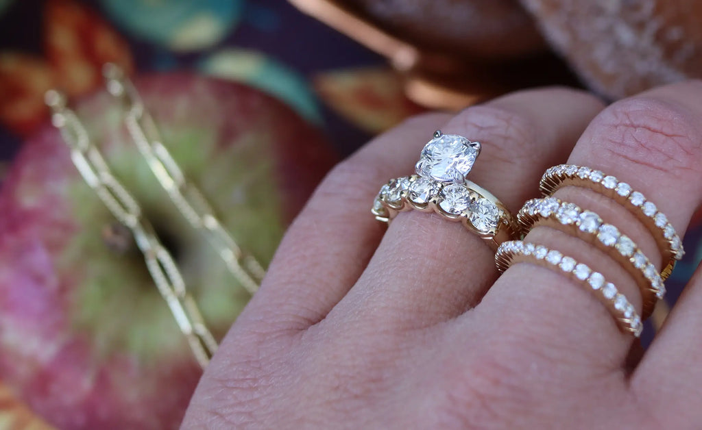 Engagement ring and wedding bands on woman's finger. Apple in background.